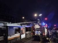 Auf dem Dach eines Löschfahrzeugs knien zwei Feuerwehrmänner und löschen das Feuer auf dem Dach der gegenüberstehenden Straßenbahn
