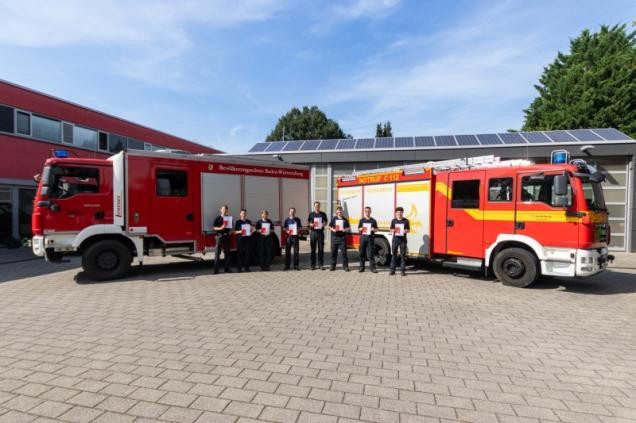 Gruppenbild zum Prüfungsende vor zwei Feuerwehrfahrzeugen
