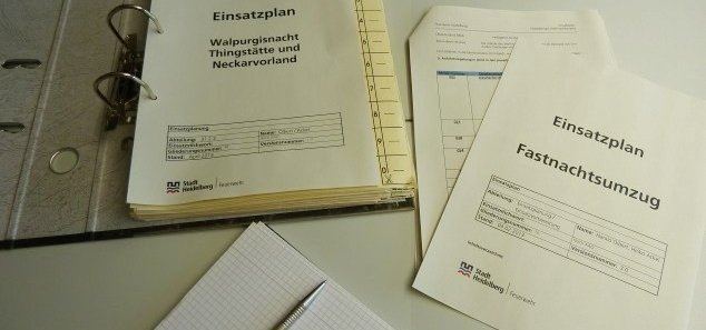 offener Leitzordner mit einem Einsatzplan, daneben ein Block mit Kugelschreiber