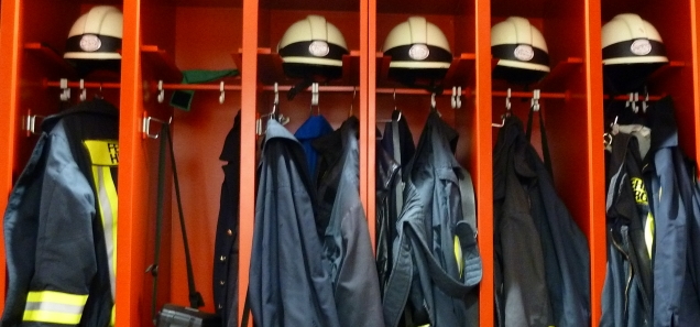 Blick auf Spinde mit Feuerwehrhelmen und Einsatzjacken